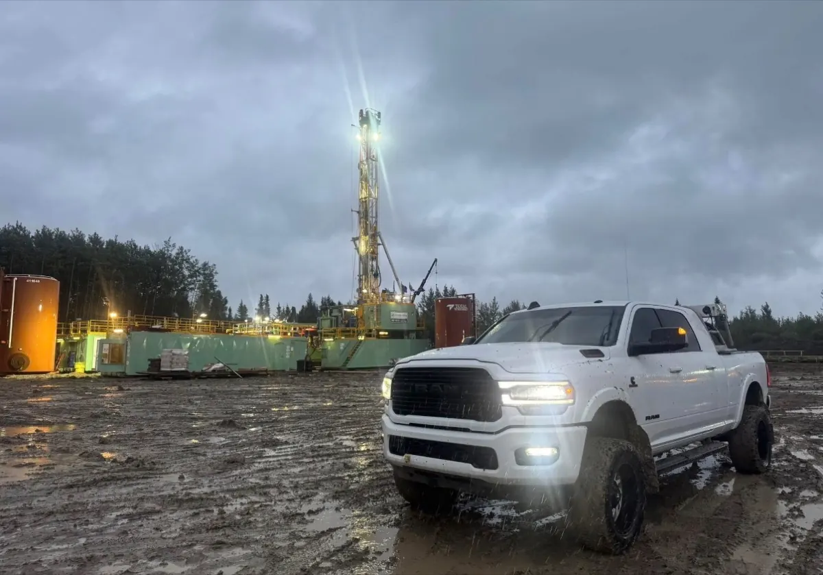 Rig Dawgs truck parked on a lease at dusk in the rain, a drilling rig lit up behind it